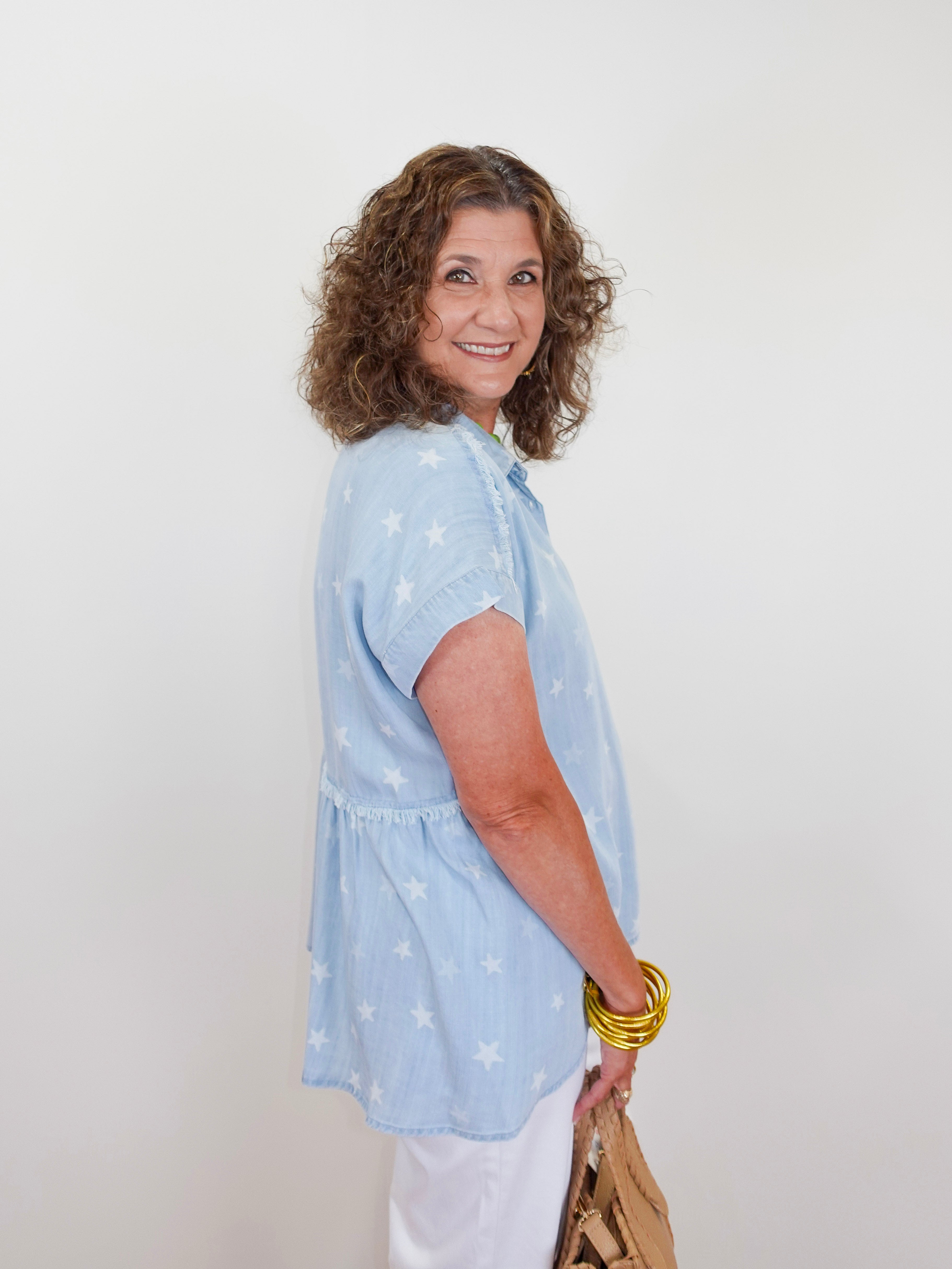 Woman wearing a light blue blouse with white patterns against a plain background