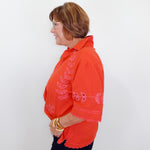Woman wearing an orange embroidered blouse against a white background