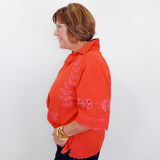 Woman wearing an orange embroidered blouse against a white background