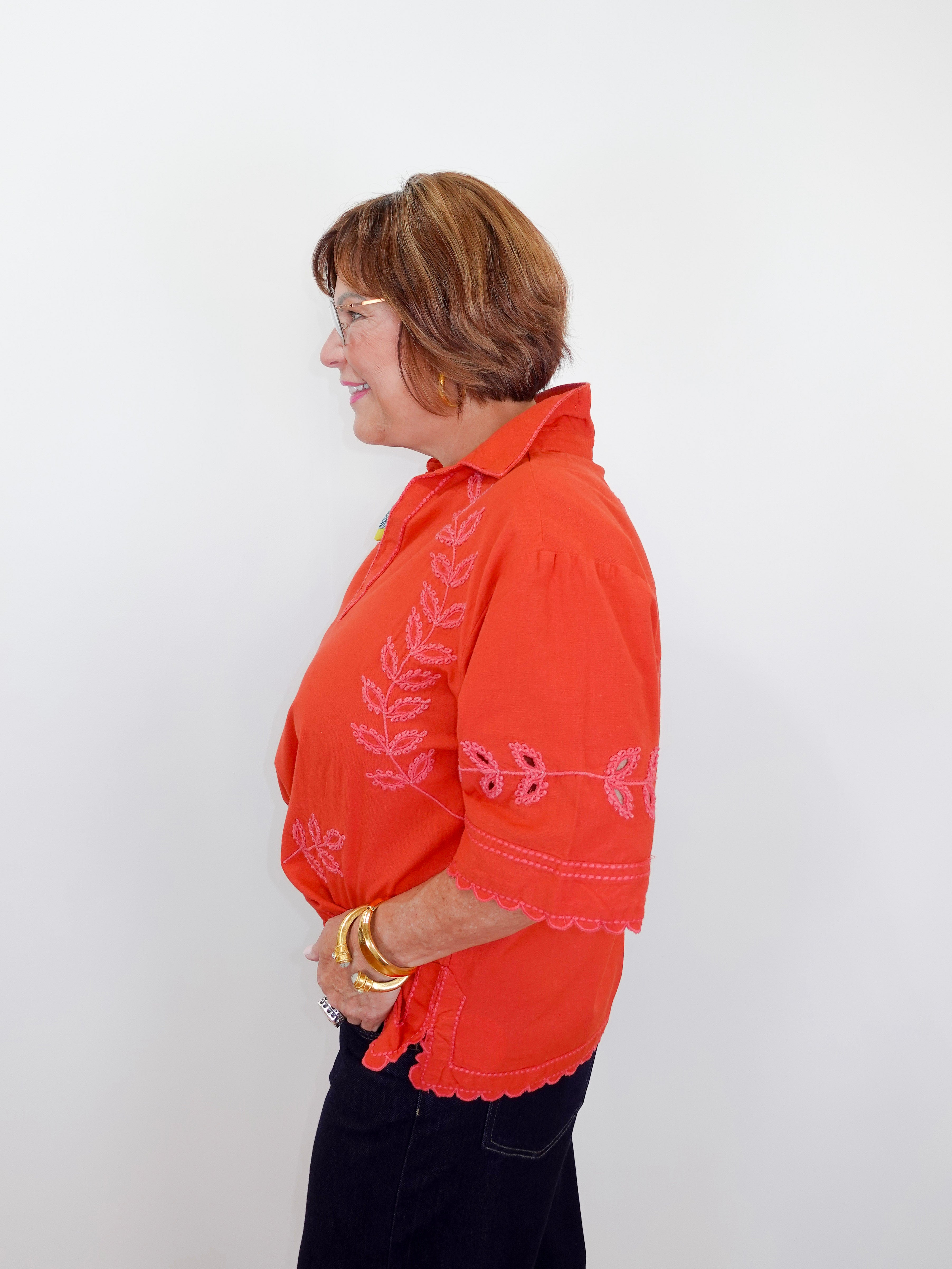Woman wearing an orange embroidered blouse against a white background