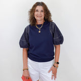 Woman wearing a navy blue top with white shorts and holding a red clutch against a white background