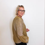 Person wearing a gold sweater and black pants against a white background