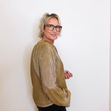 Person wearing a gold sweater and black pants against a white background