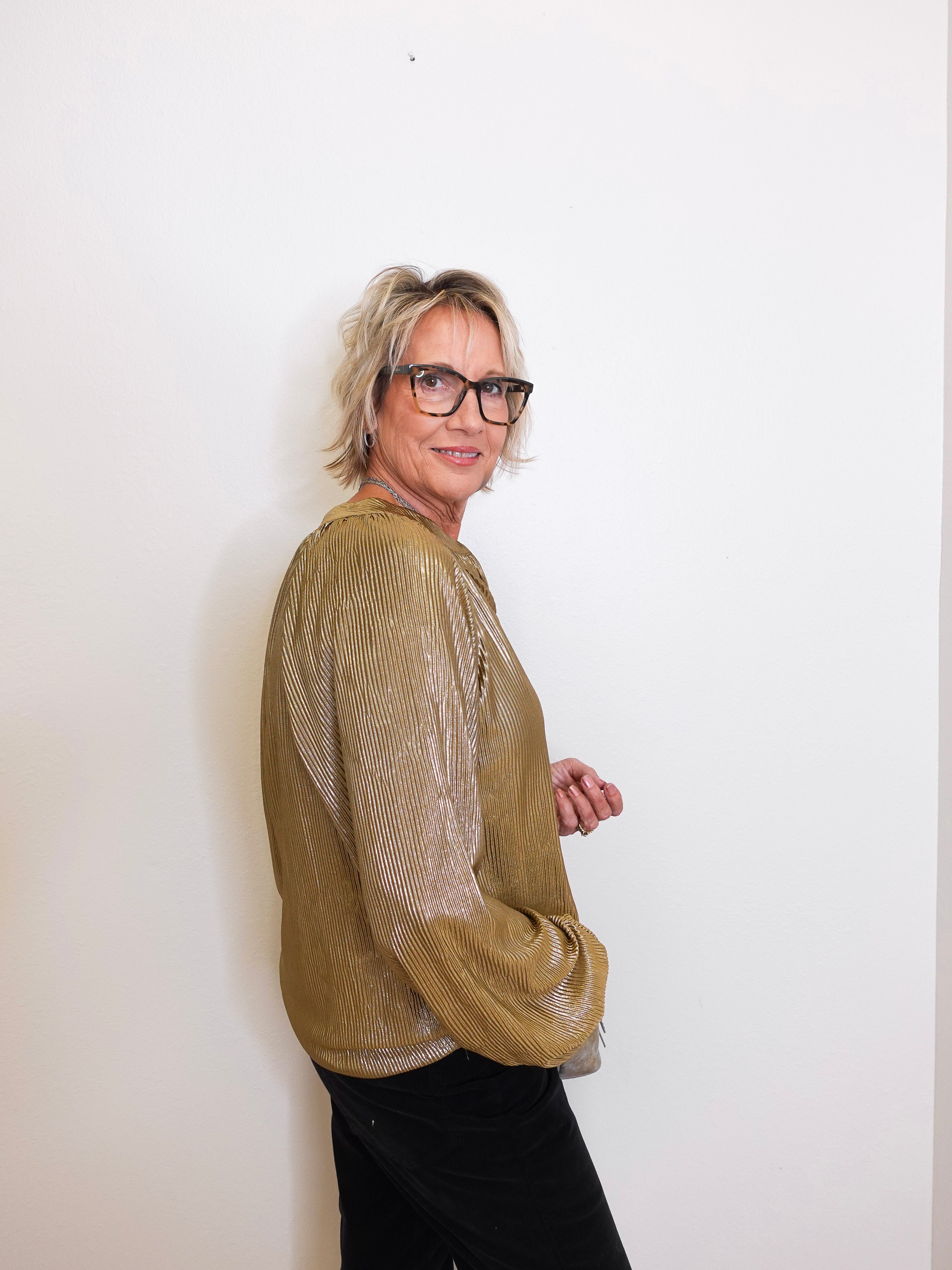 Person wearing a gold sweater and black pants against a white background