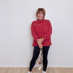 Woman wearing a red sweater and black leggings standing against a white wall.