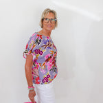 Woman wearing a floral blouse and white pants against a white background
