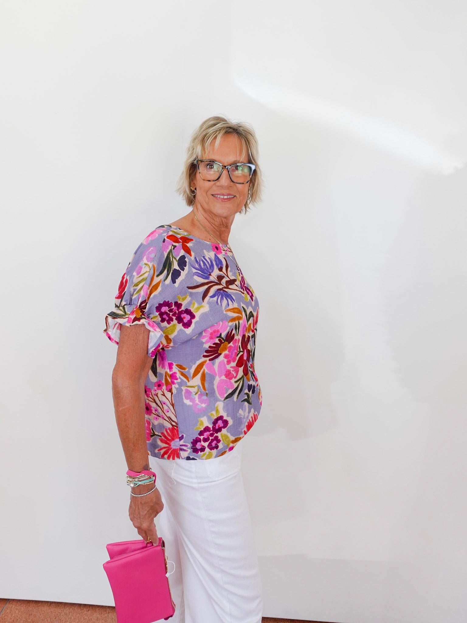 Woman wearing a floral blouse and white pants against a white background