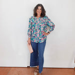 Woman wearing a floral blouse and blue jeans standing against a white wall.
