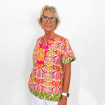 Woman wearing a colorful patterned blouse and white pants on a white background
