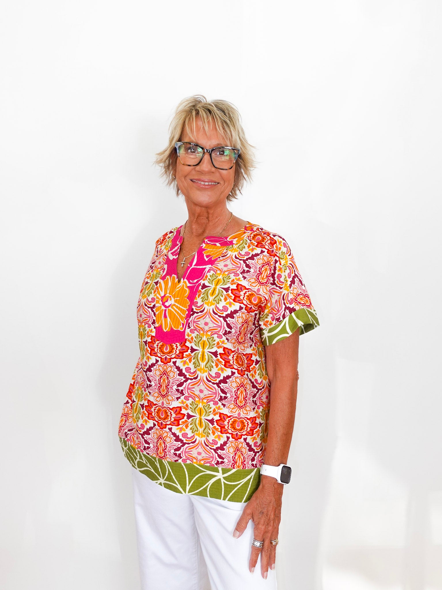 Woman wearing a colorful patterned blouse and white pants on a white background