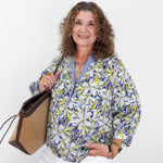 Woman holding a handbag wearing a patterned blouse against a white background