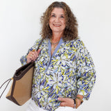 Woman holding a handbag wearing a patterned blouse against a white background