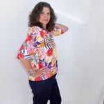 Woman wearing a colorful floral blouse and dark pants against a white background