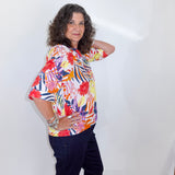 Woman wearing a colorful floral blouse and dark pants against a white background