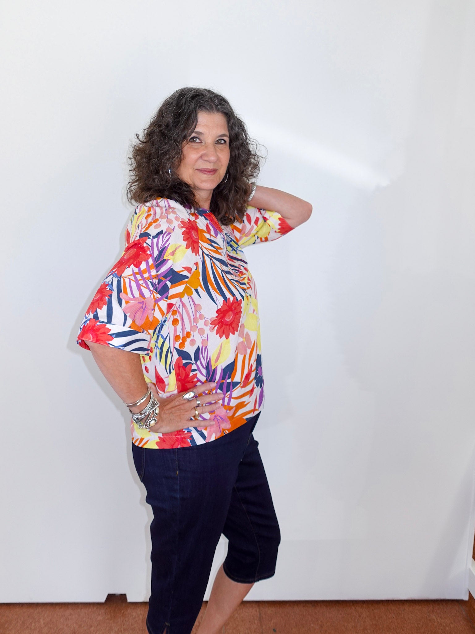 Woman wearing a colorful floral blouse and dark pants against a white background