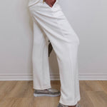 Person wearing white pants and gray sneakers on a light wooden floor.