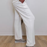 Person wearing white pants and gray sneakers on a light wooden floor.