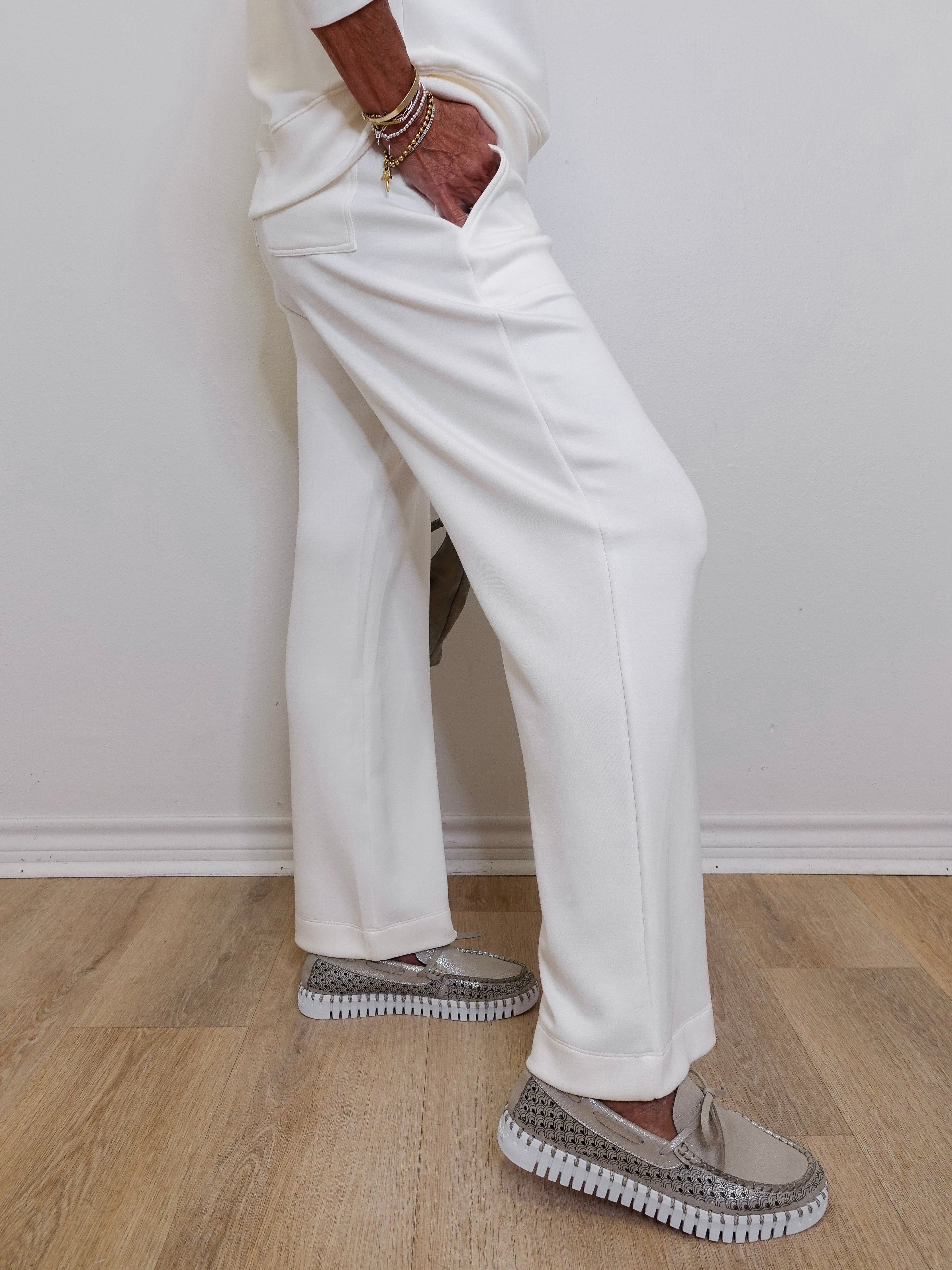 Person wearing white pants and gray sneakers on a light wooden floor.