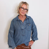 Person wearing a blue denim shirt and brown pants against a white background