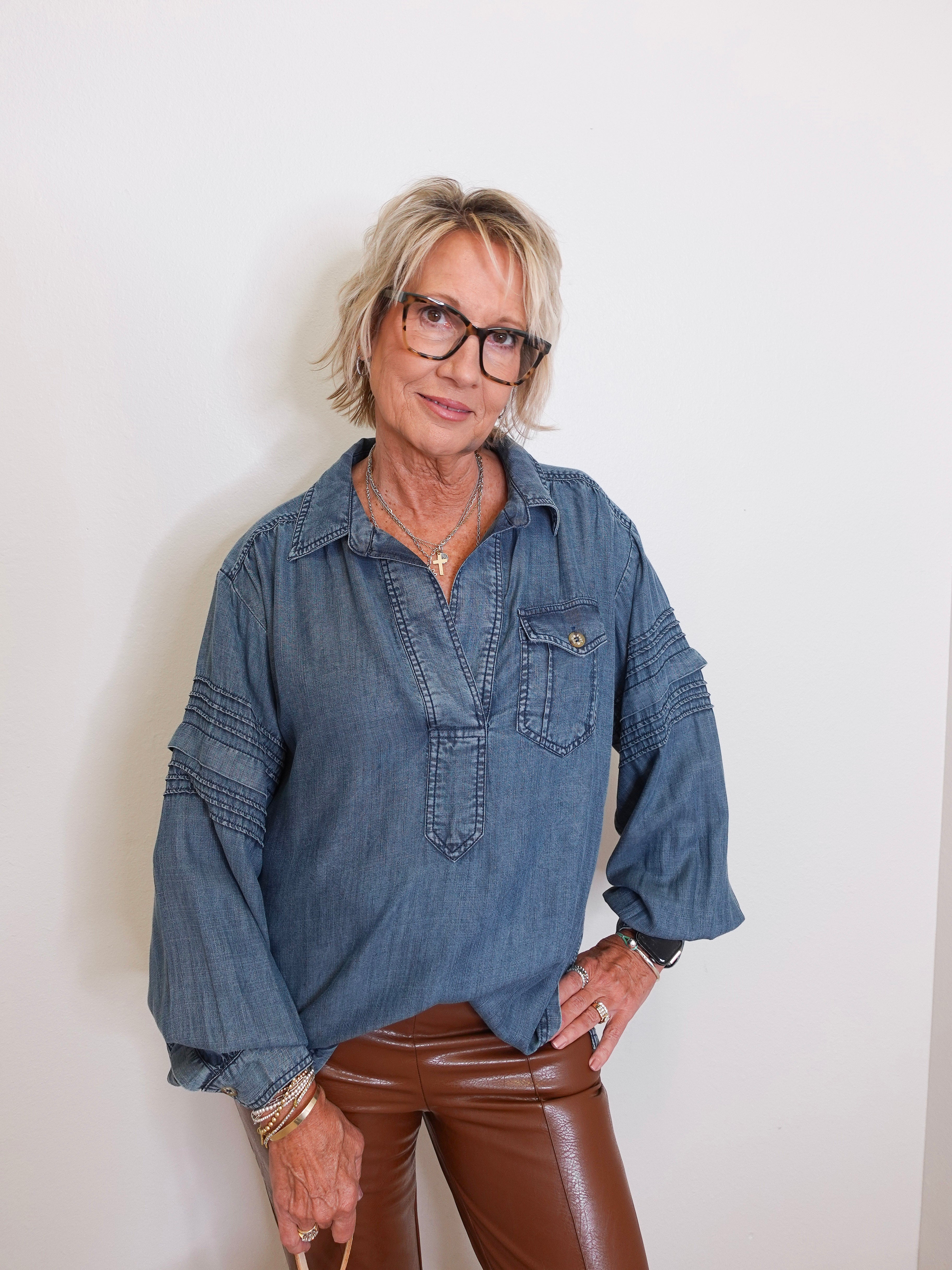 Person wearing a blue denim shirt and brown pants against a white background