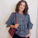 Woman wearing a blue patterned blouse and holding a red bag against a white wall