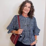 Woman wearing a blue patterned blouse and holding a red bag against a white wall