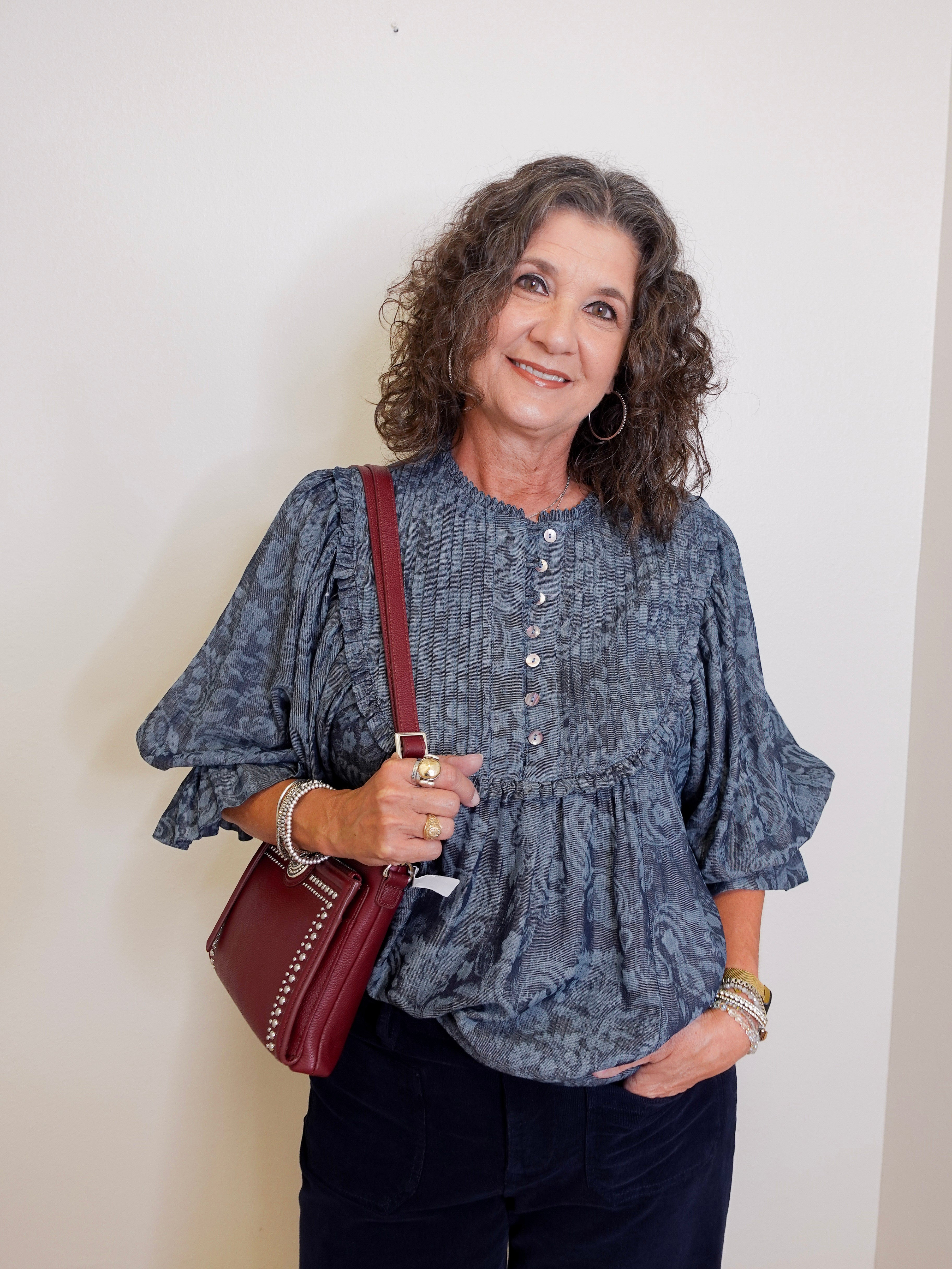 Woman wearing a blue patterned blouse and holding a red bag against a white wall