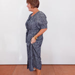 Woman wearing a blue patterned dress standing against a white wall.