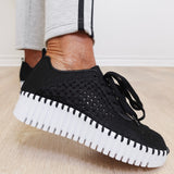 Black knitted sneakers with white soles worn by a person on a light wooden floor.
