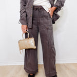Person wearing a gray jacket and pants holding a beige handbag against a white background