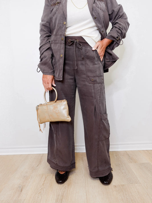 Person wearing a gray jacket and pants holding a beige handbag against a white background