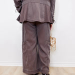 Person wearing a gray outfit with wide-leg pants against a white wall.