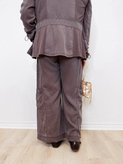 Person wearing a gray outfit with wide-leg pants against a white wall.