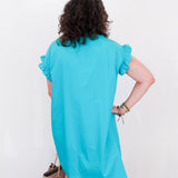 Person wearing a turquoise dress with ruffled sleeves against a white background