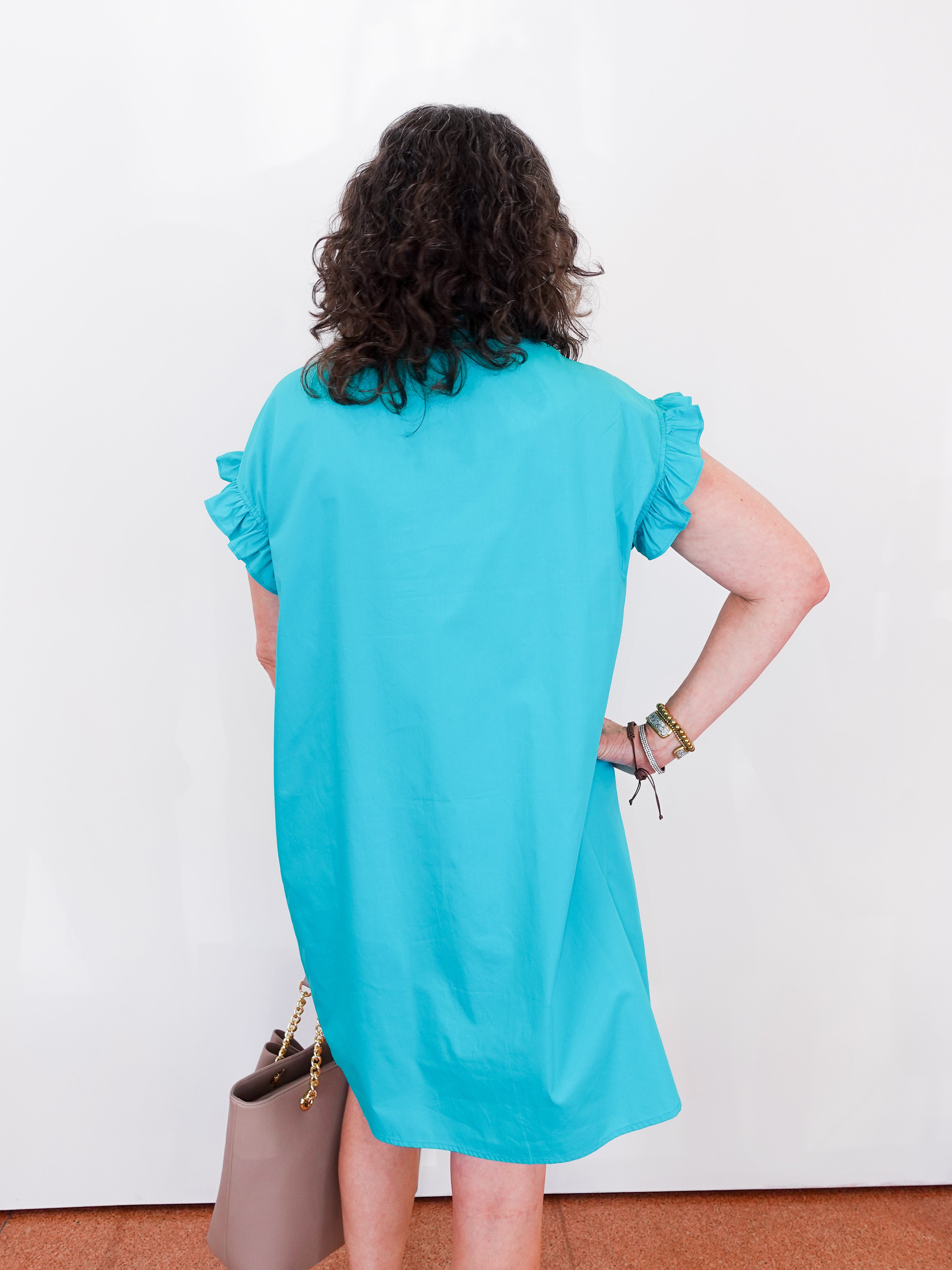 Person wearing a turquoise dress with ruffled sleeves against a white background