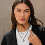 Woman wearing layered necklaces and a ring against a neutral background