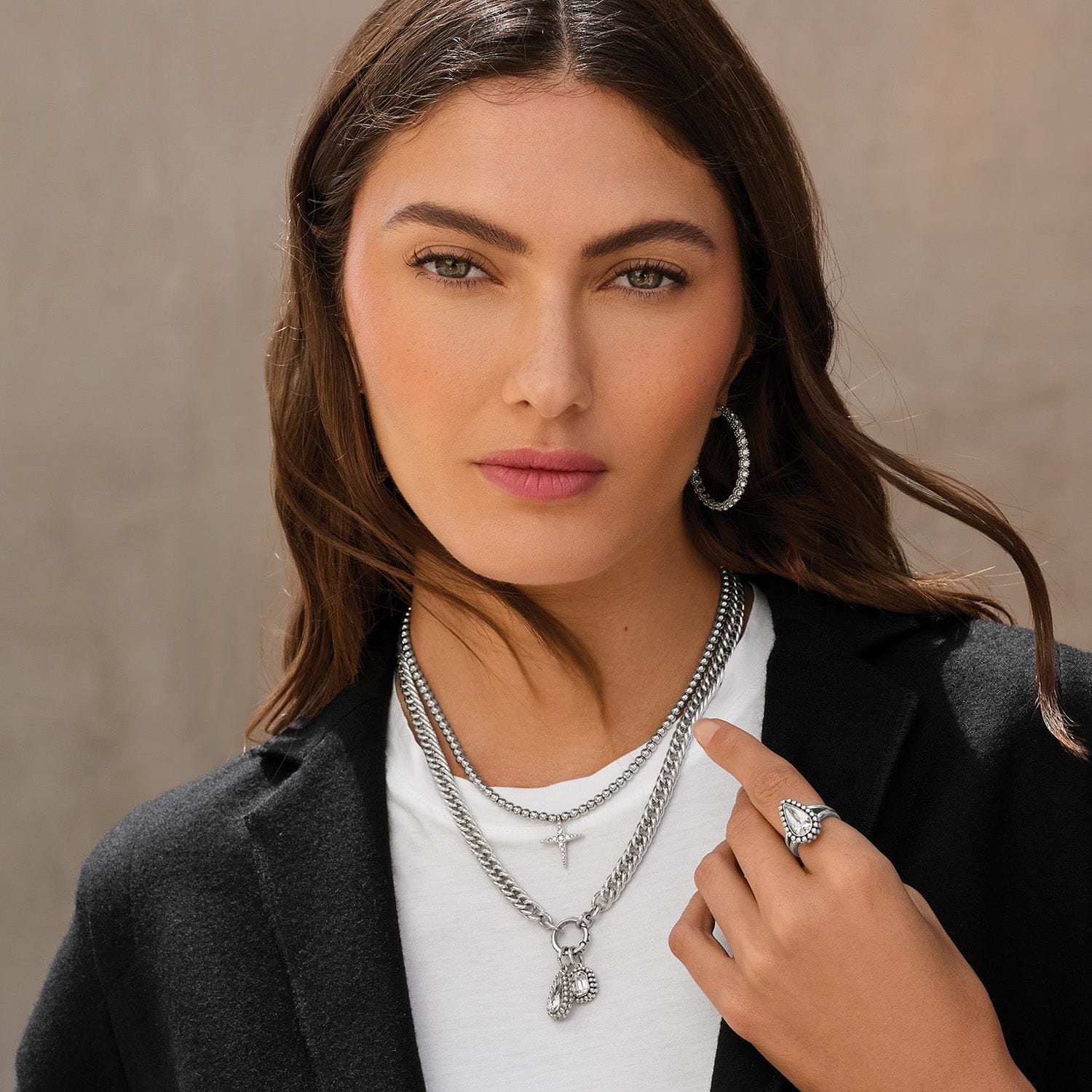 Woman wearing layered necklaces and a ring against a neutral background