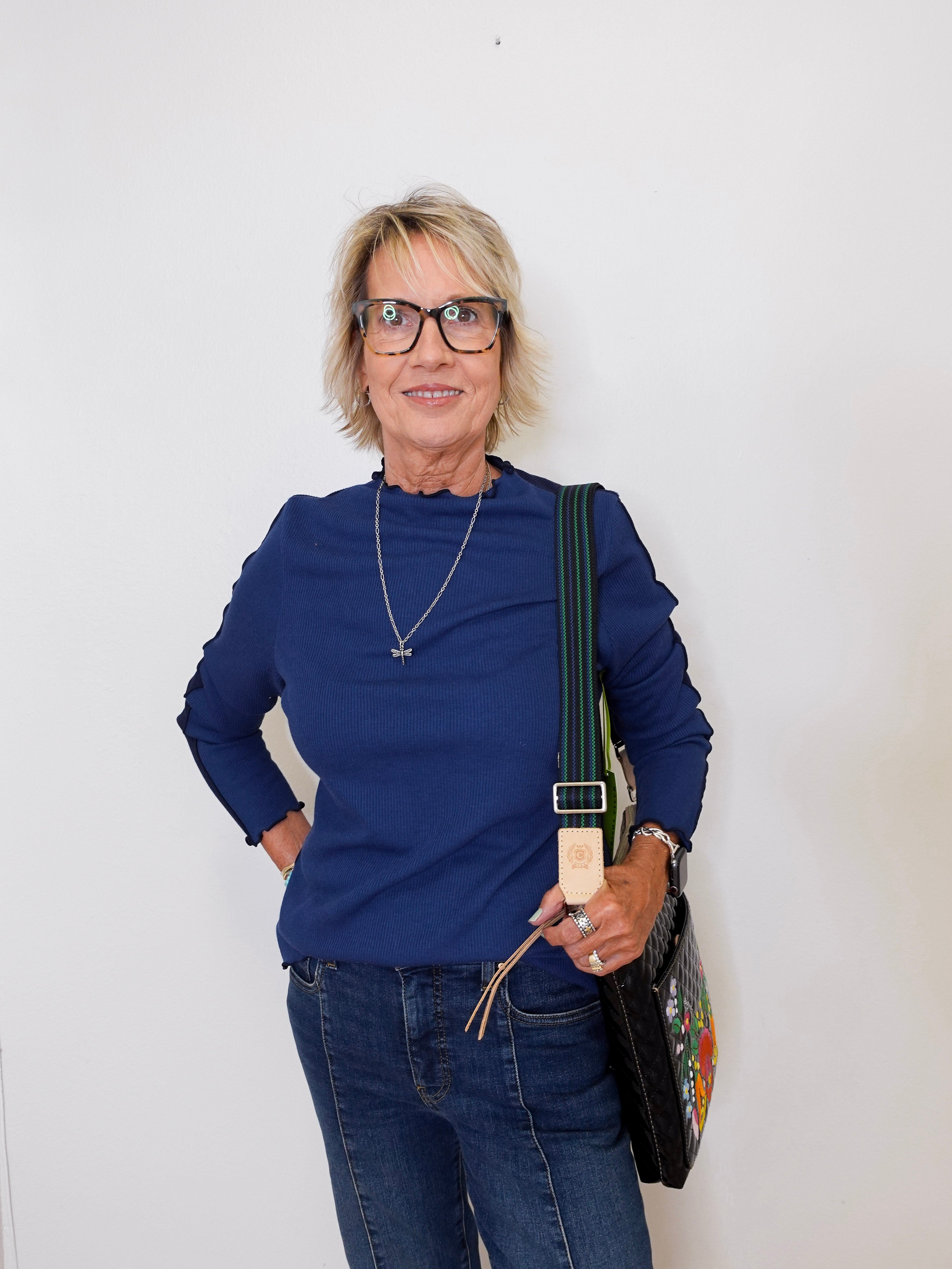 Woman wearing a blue top and jeans, holding a bag against a white background