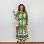 Woman wearing a green dress with white patterns, holding a white bag against a white background.