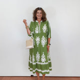 Woman wearing a green dress with white patterns, holding a white bag against a white background.