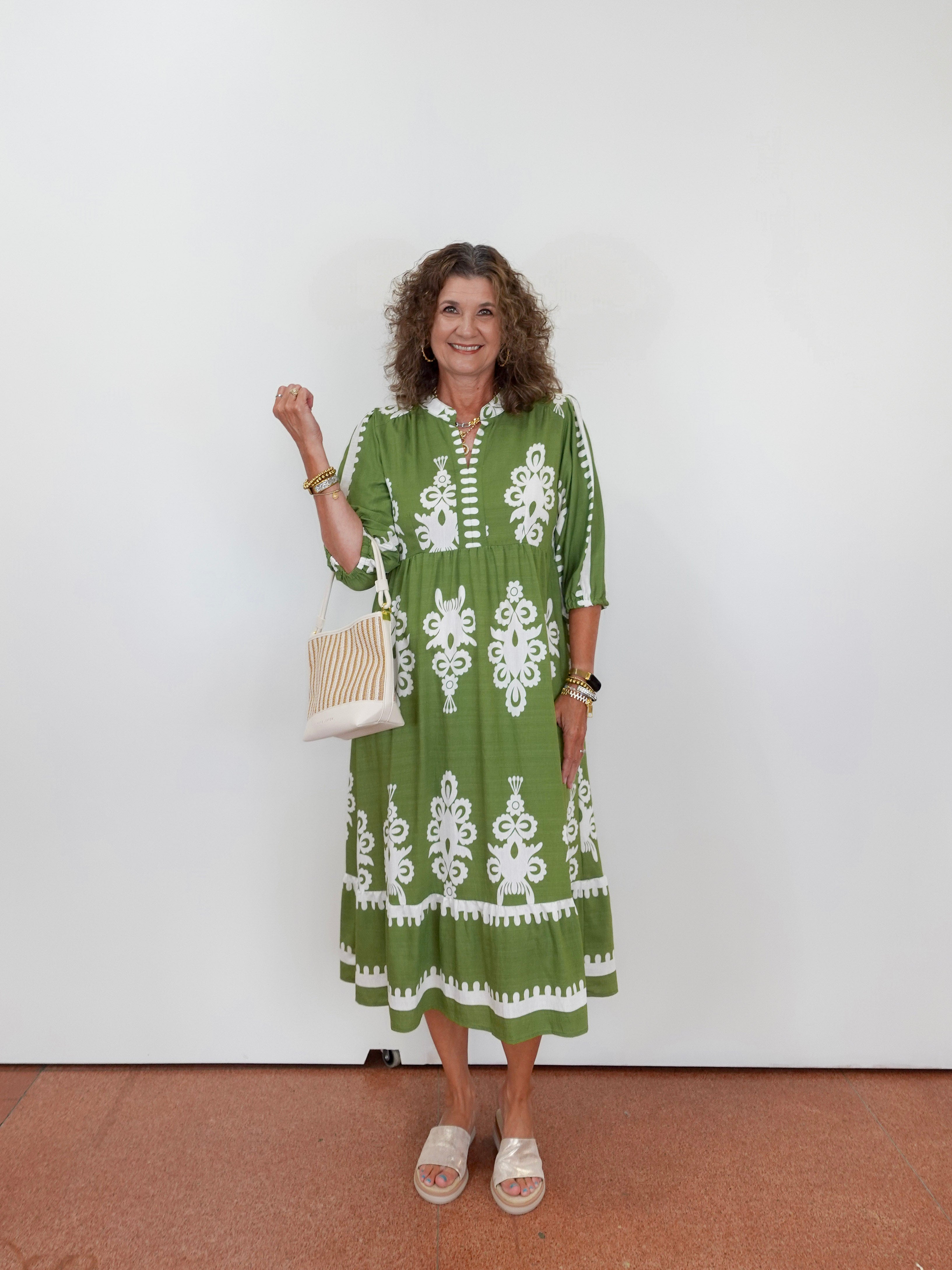 Woman wearing a green dress with white patterns, holding a white bag against a white background.