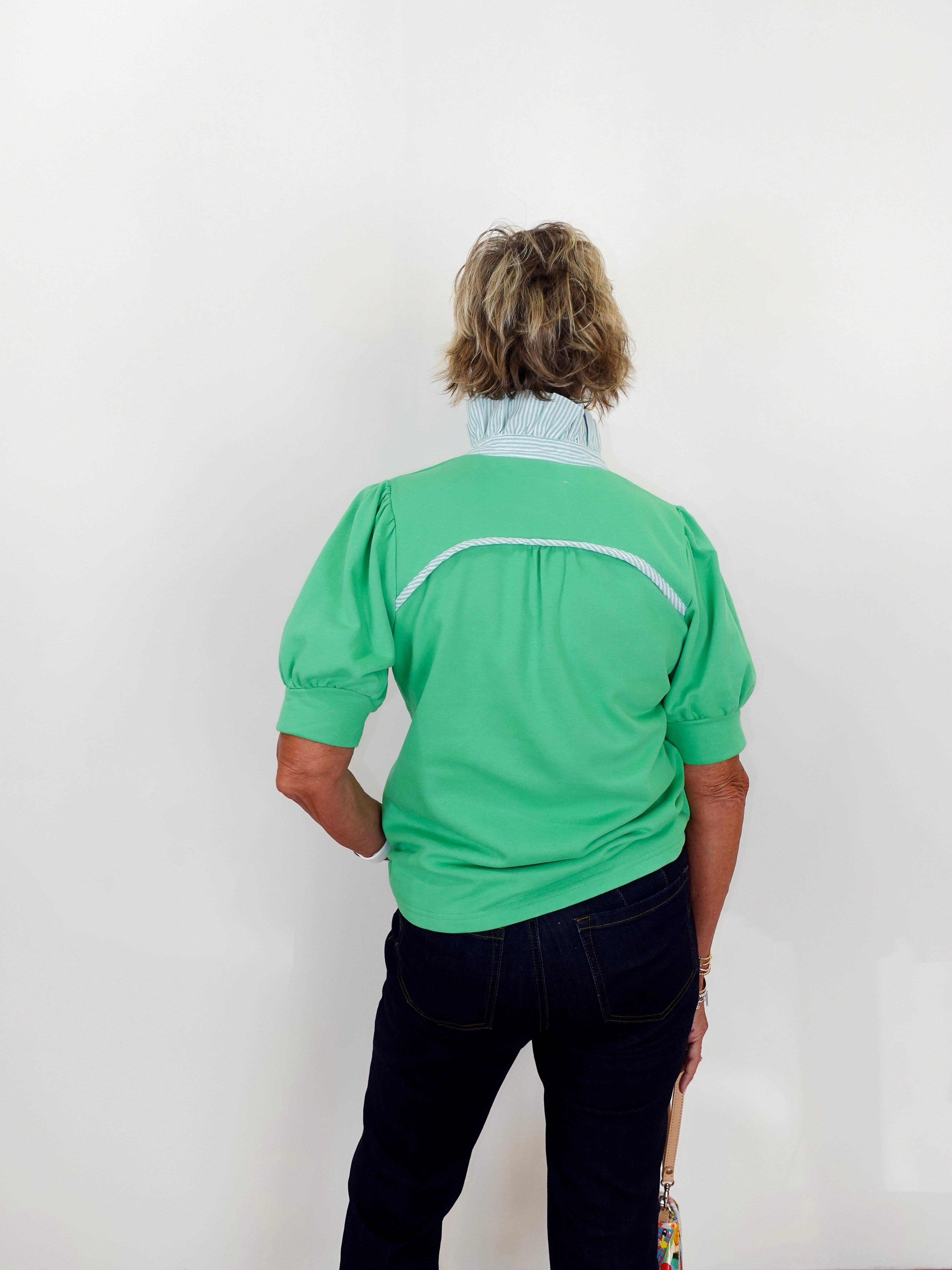 Person wearing a green shirt with a white stripe on a plain background