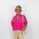 Woman wearing a bright pink blouse with colorful sleeves on a white background