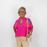 Woman wearing a bright pink blouse with colorful sleeves on a white background