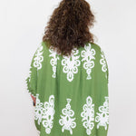 Person wearing a green patterned top with white designs on a white background