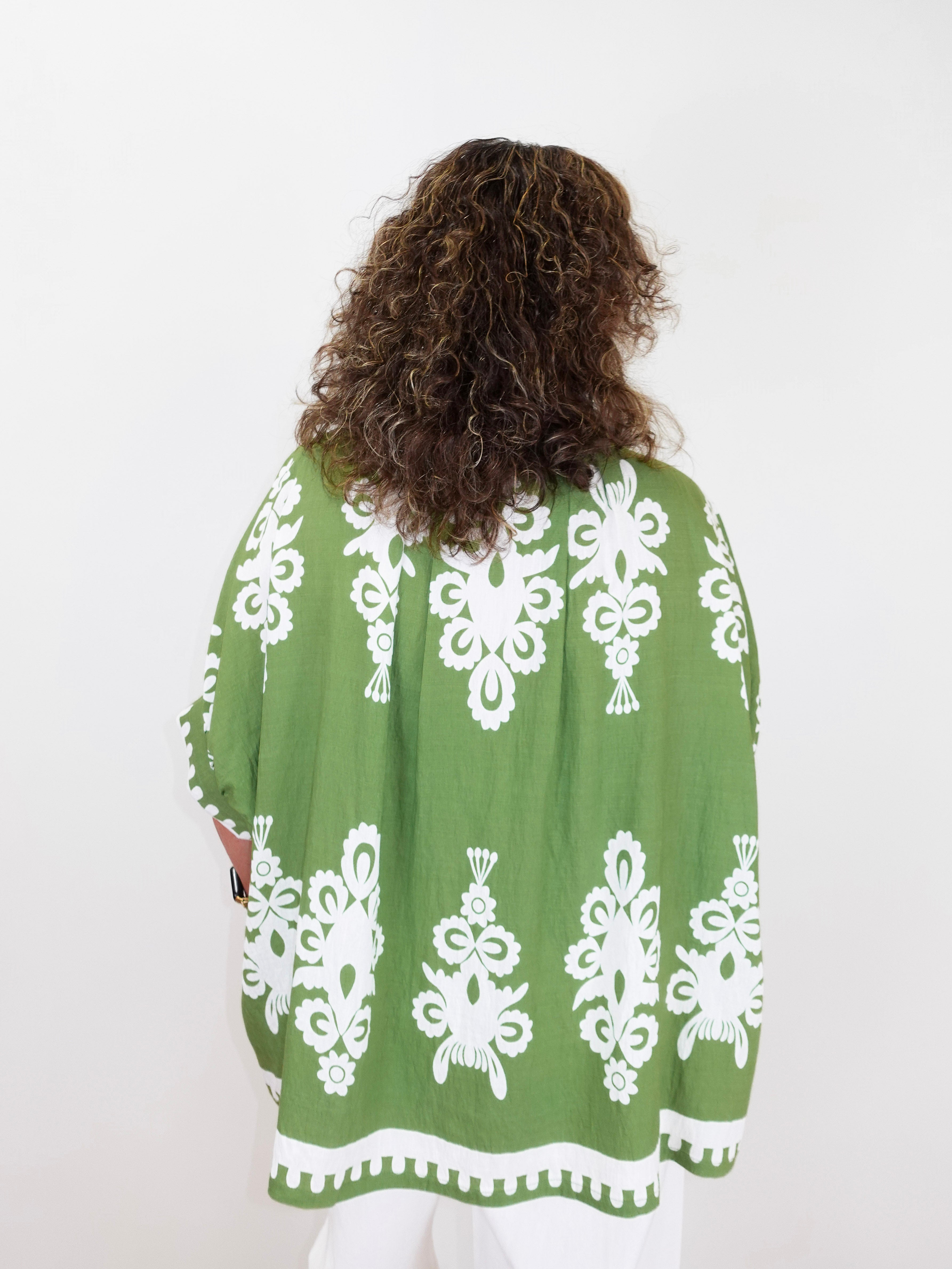 Person wearing a green patterned top with white designs on a white background