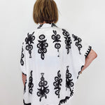 Person wearing a white poncho with black floral patterns against a white background