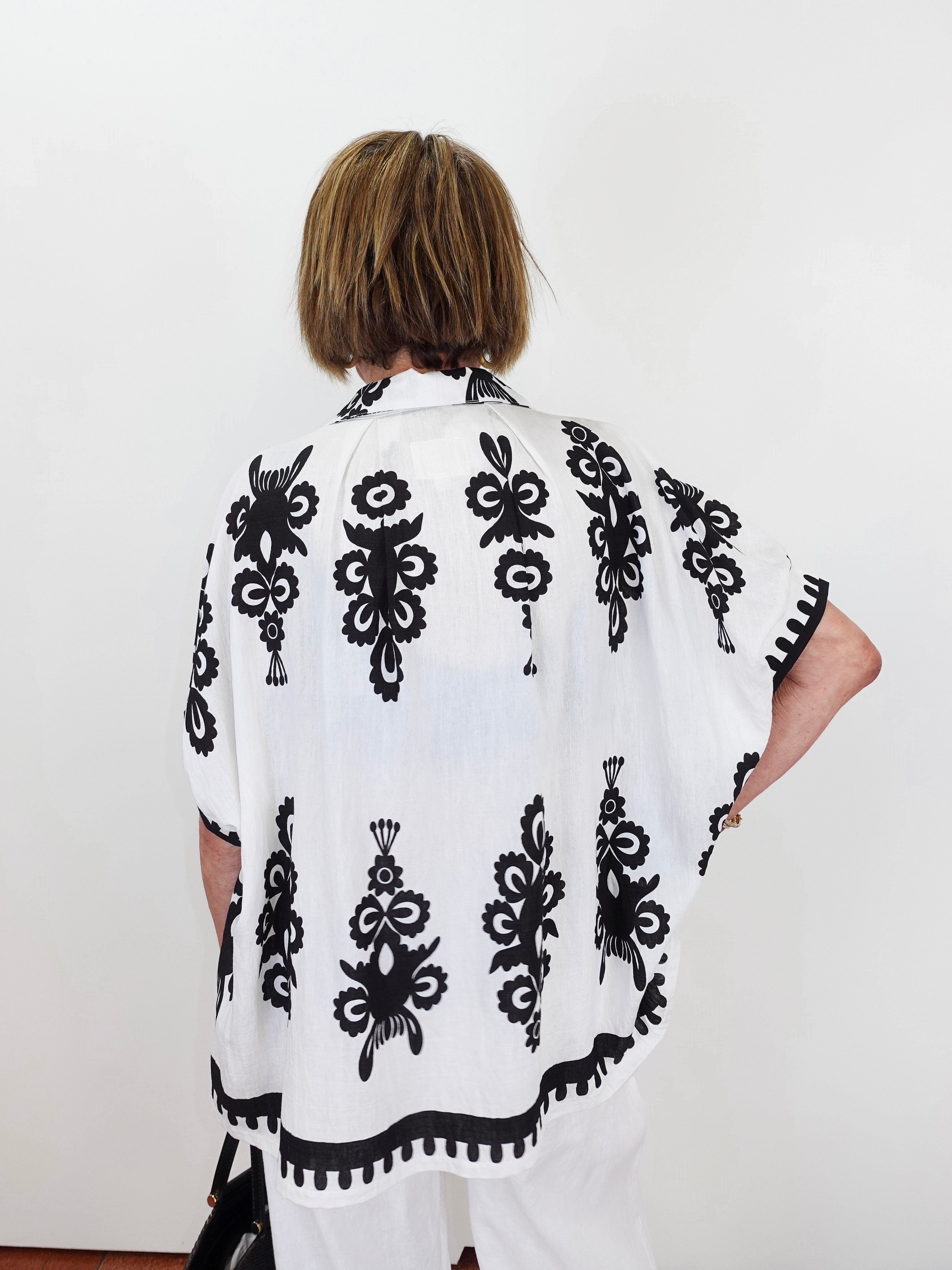 Person wearing a white poncho with black floral patterns against a white background