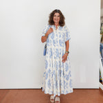 Woman wearing a floral dress standing against a white wall.