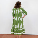 Woman wearing a green dress with white patterns standing against a white wall.